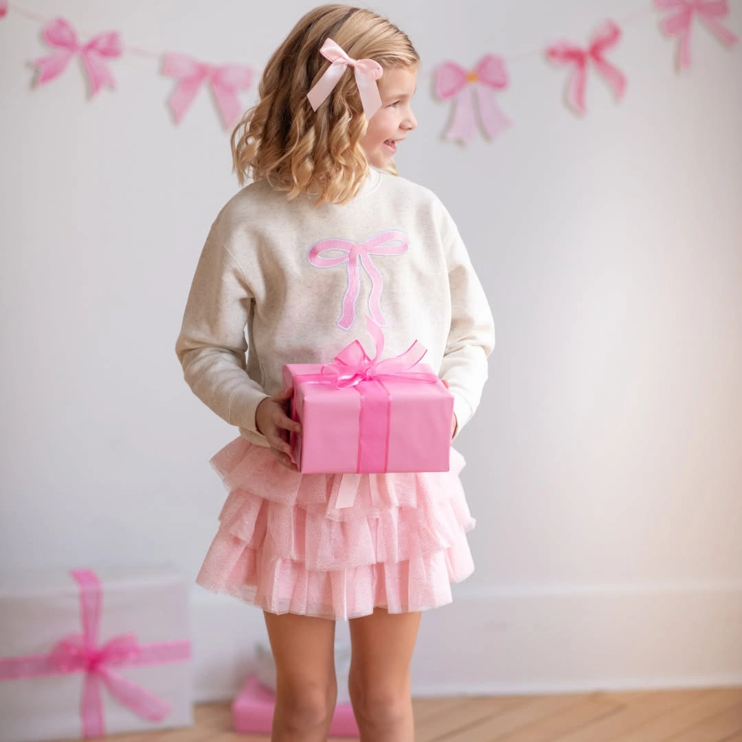 Child in white bow sweater and pink tiered skirt