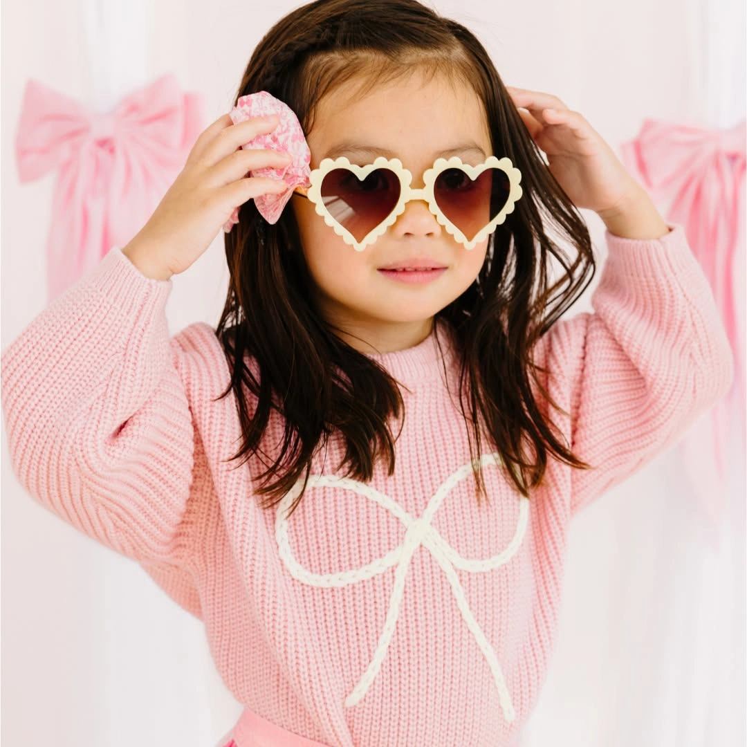 Child in pink knit sweater wearing heart shaped sunglasses