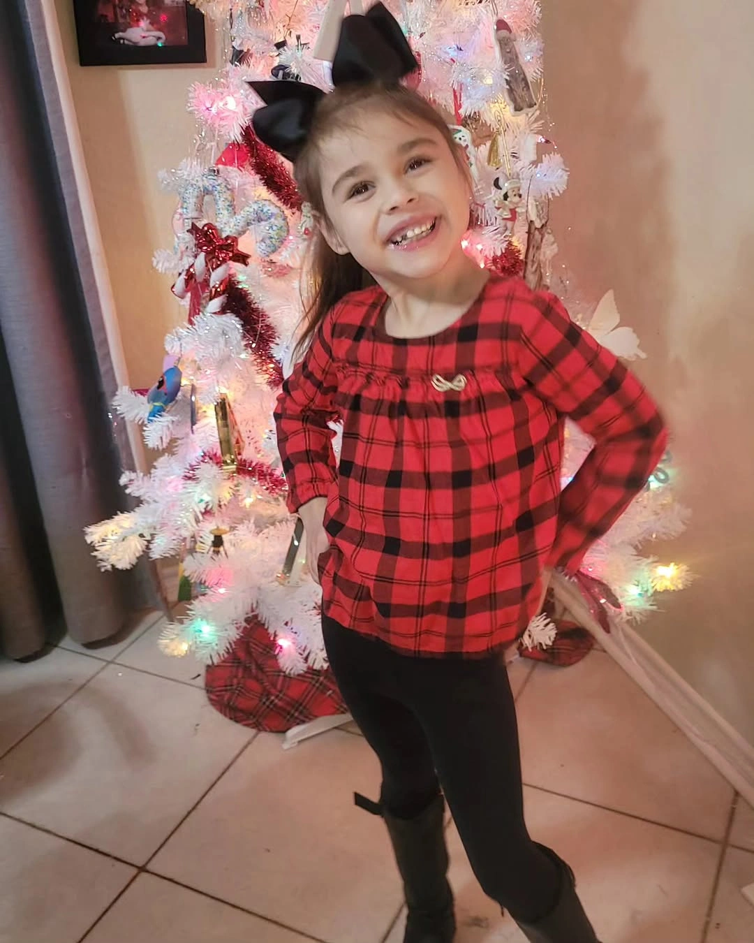 Child wearing red plaid top black leggings and bow