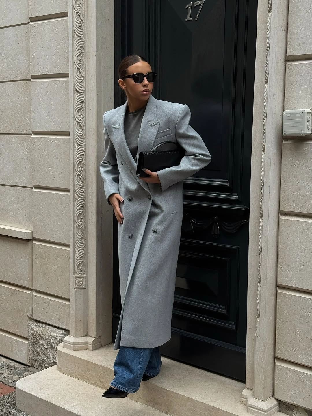 Light gray double-breasted jacket with jeans and black clutch