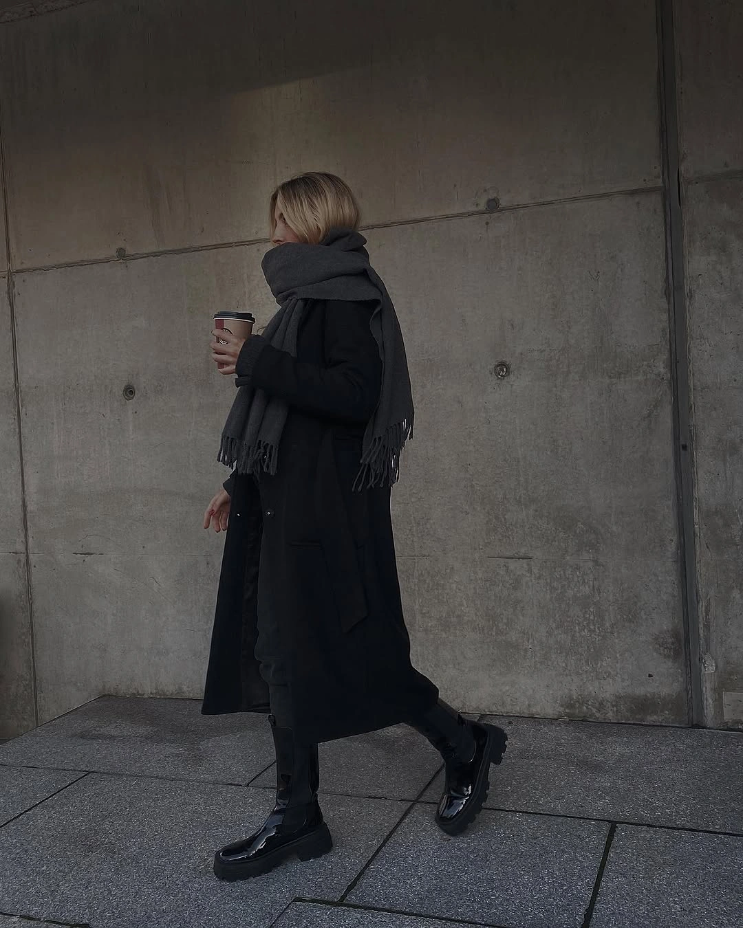 Black long coat, large scarf, dark trousers, chunky footwear