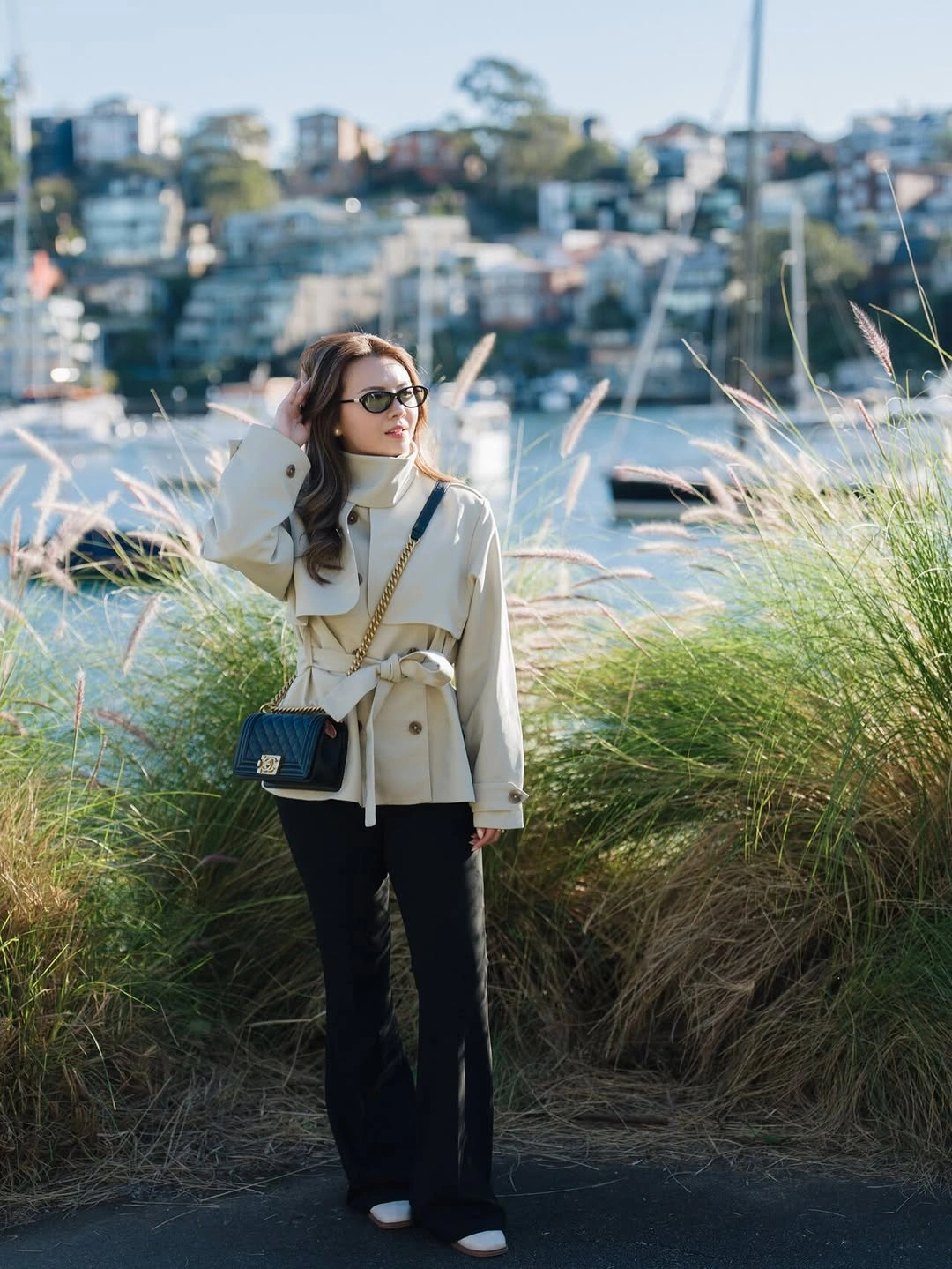 Cream belted jacket, black trousers, dark bag, and sunglasses
