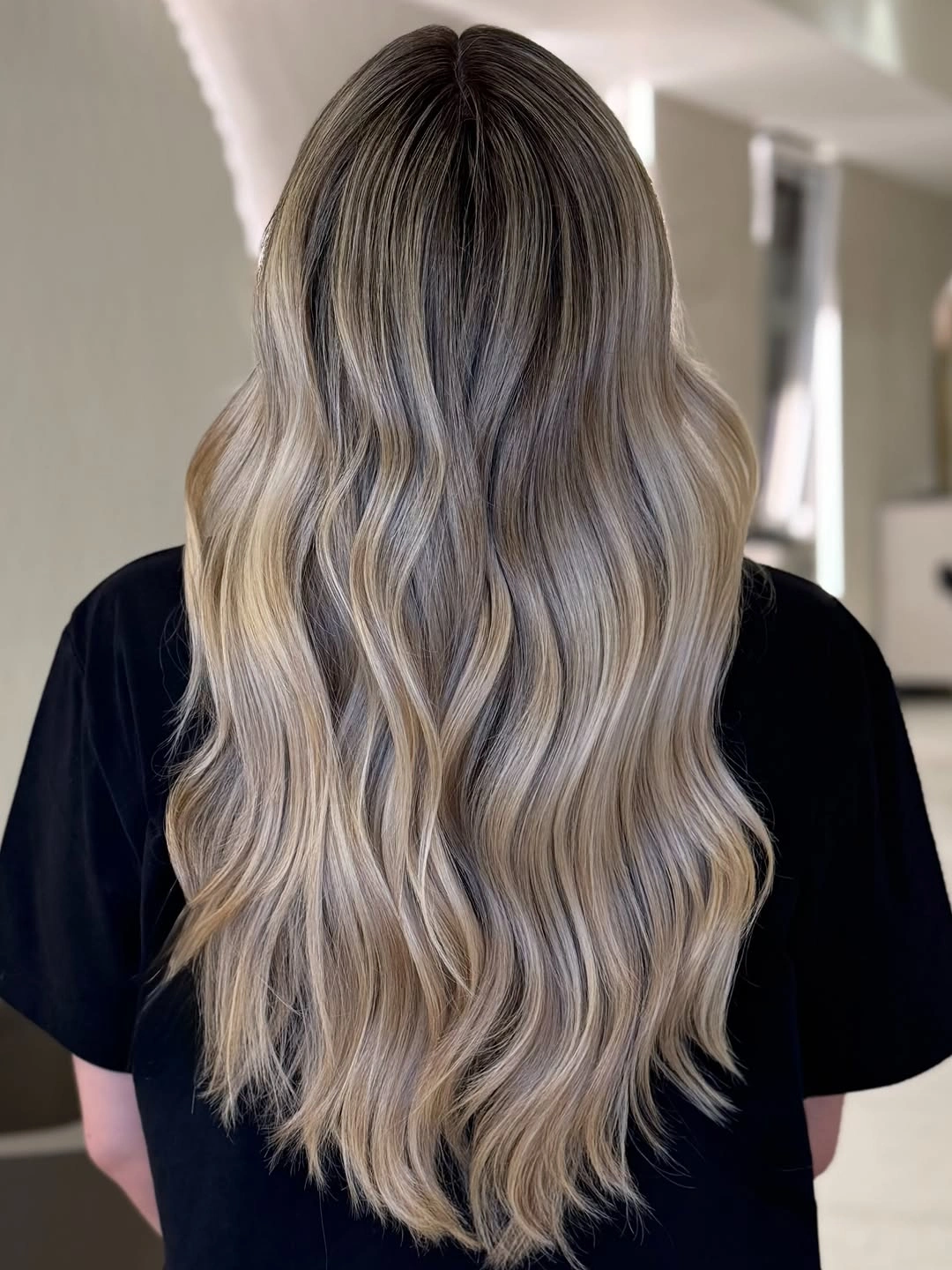 Long ash-beige blonde hair with darker upper tones and loose waves.