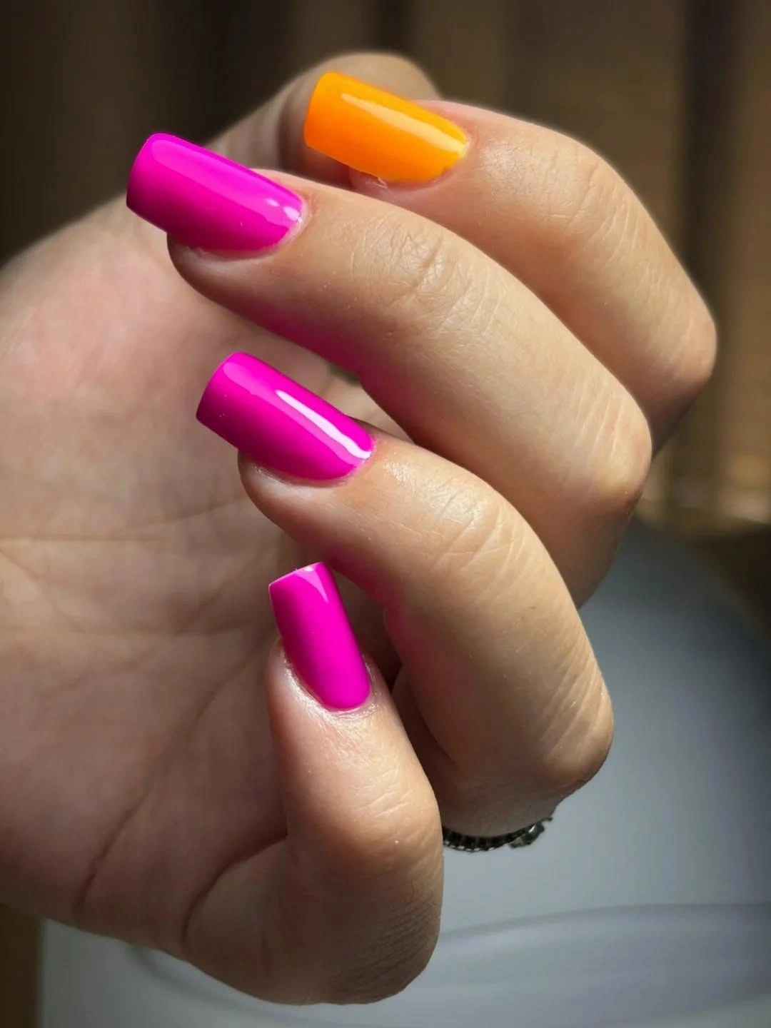 Short square fuchsia nails with one glossy orange accent