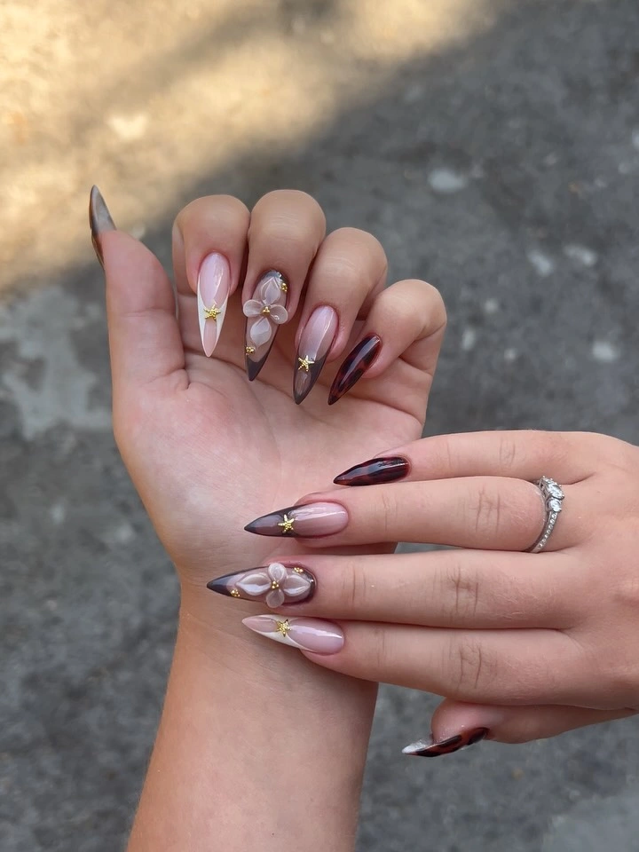 Pointed sheer pink nails with brown tips and flower-like accents
