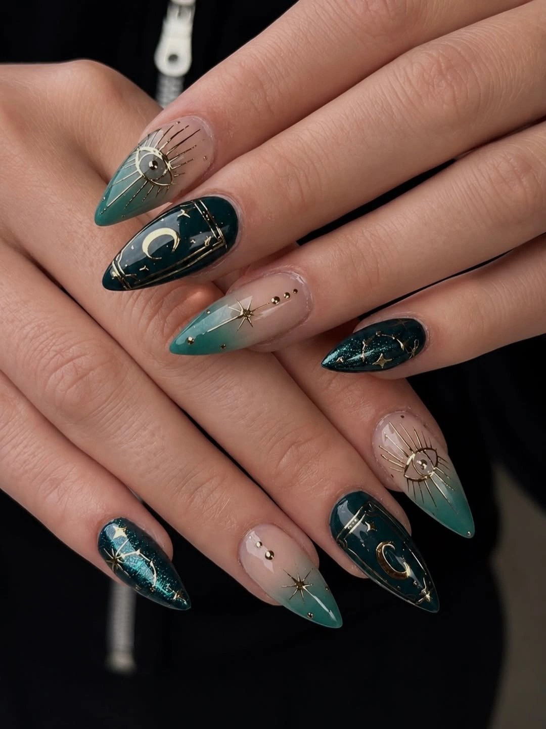 Teal almond nails with gold-colored moons and sunburst-like lines
