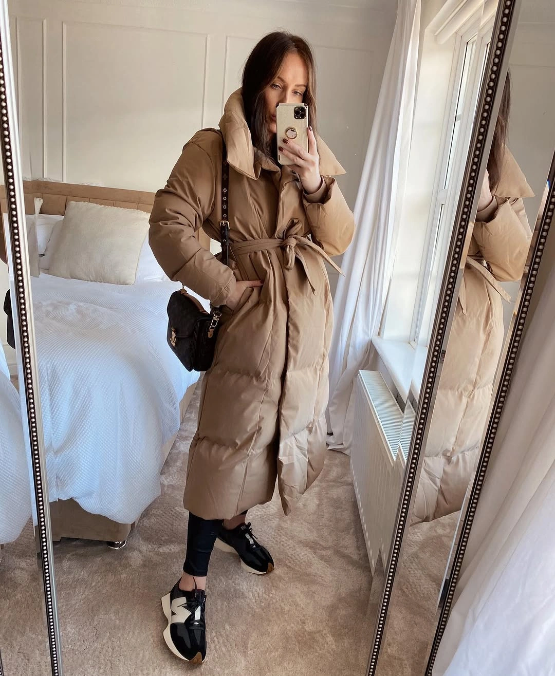 Beige belted padded-looking coat with black sneakers and crossbody bag