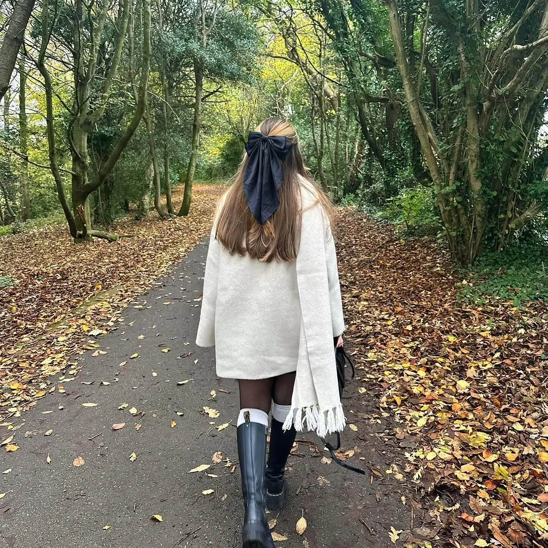 Cream long outer layer with white scarf, tall boots and black bow