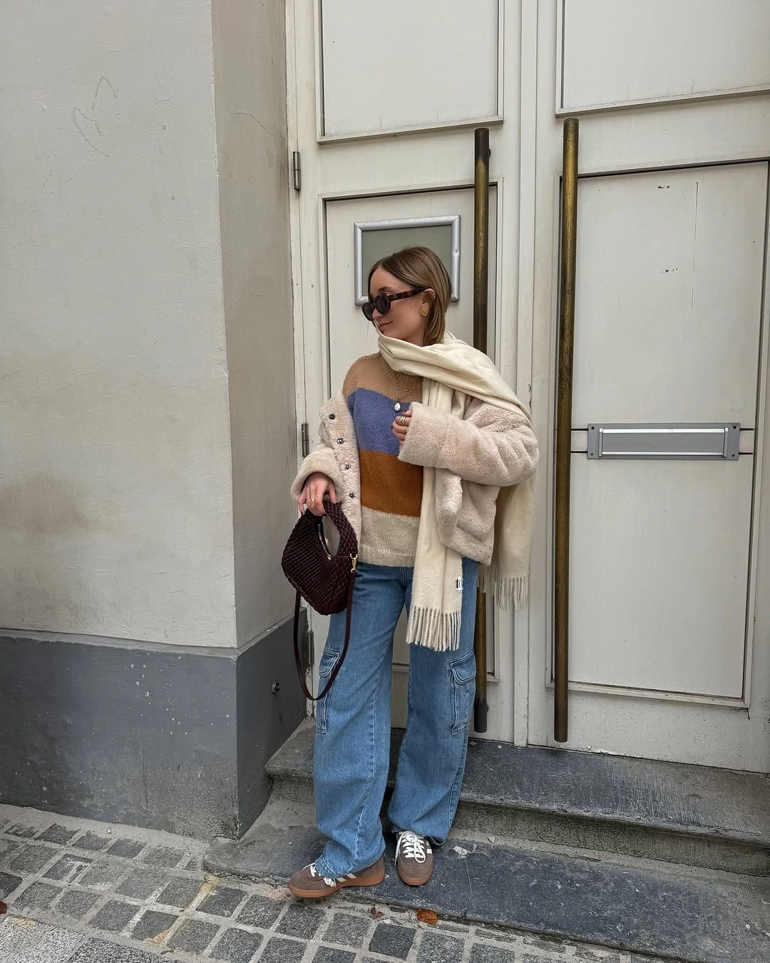 Cream layers with color block knit, blue jeans and burgundy bag