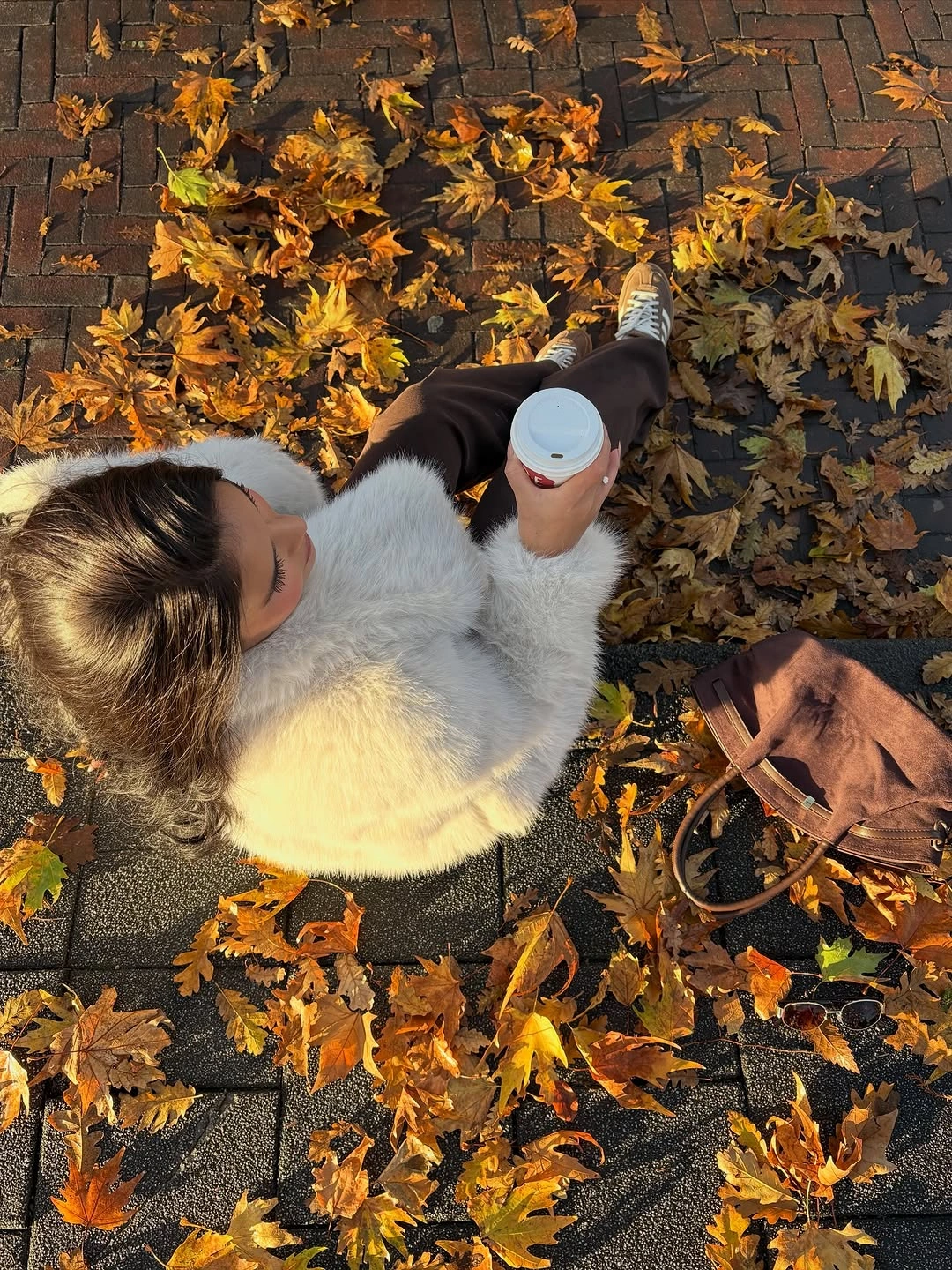 Fluffy-looking white jacket with dark pants, sneakers and coffee cup