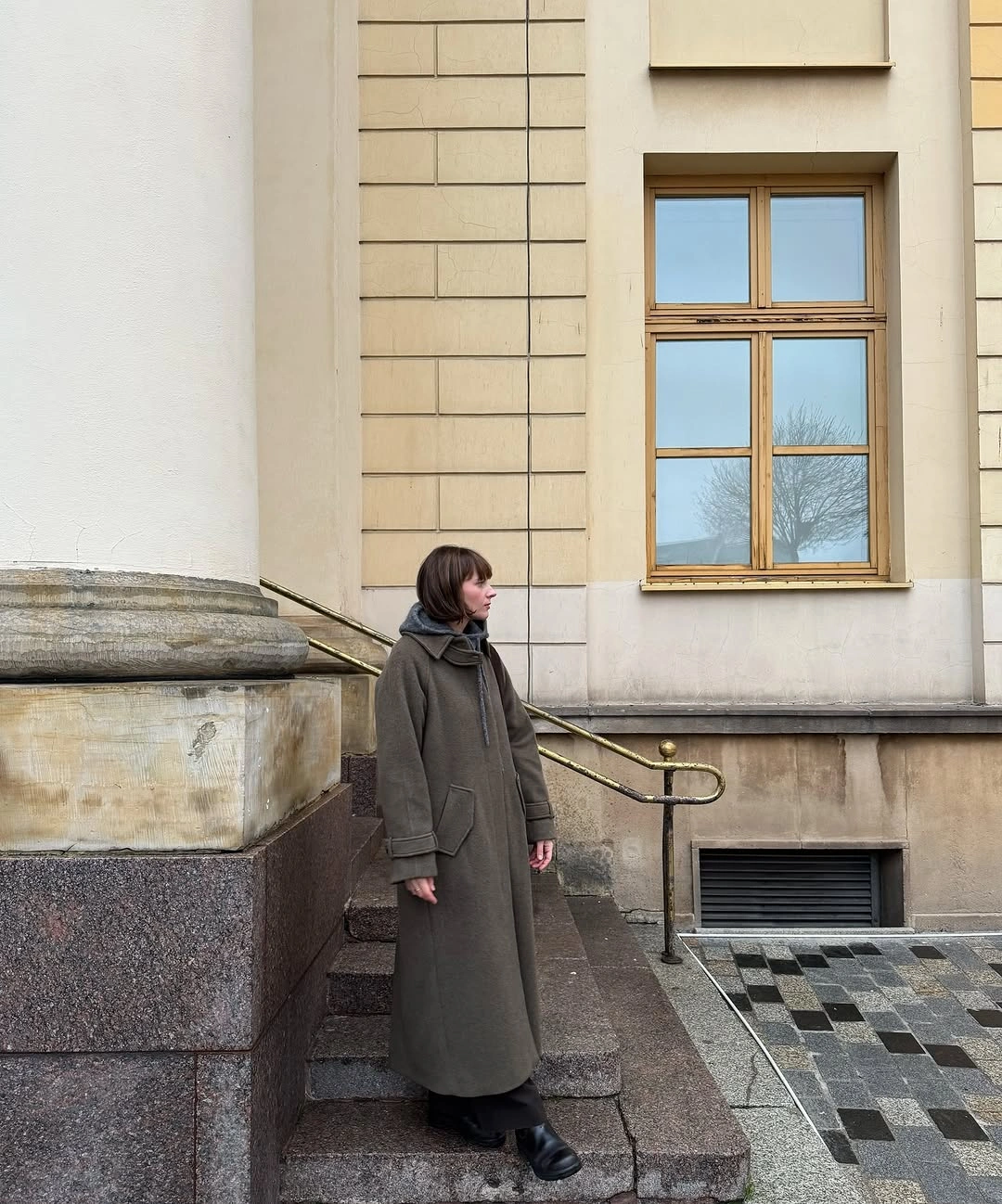 Long olive-gray coat with dark neck layer and black footwear