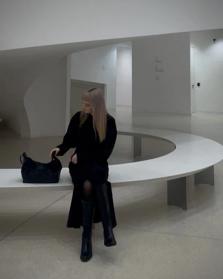 Long black outfit with tall boots and dark handbag on bench