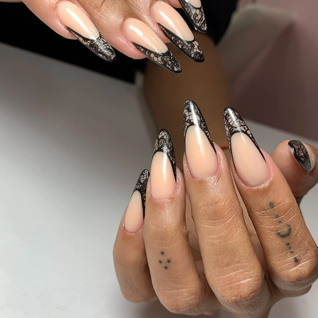 Long nude almond nails with black lace-like patterned tips