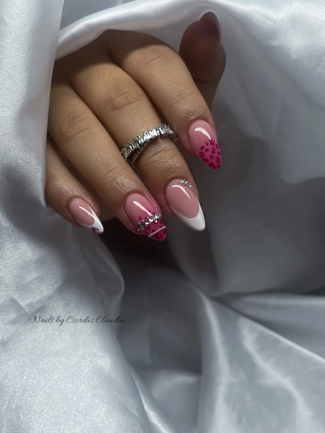 Pink almond nails with white tips, dots, and rhinestone-like detail