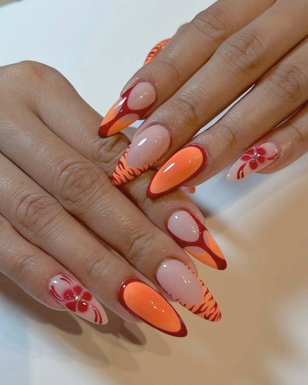 Orange almond nails with curved tips and small floral accents