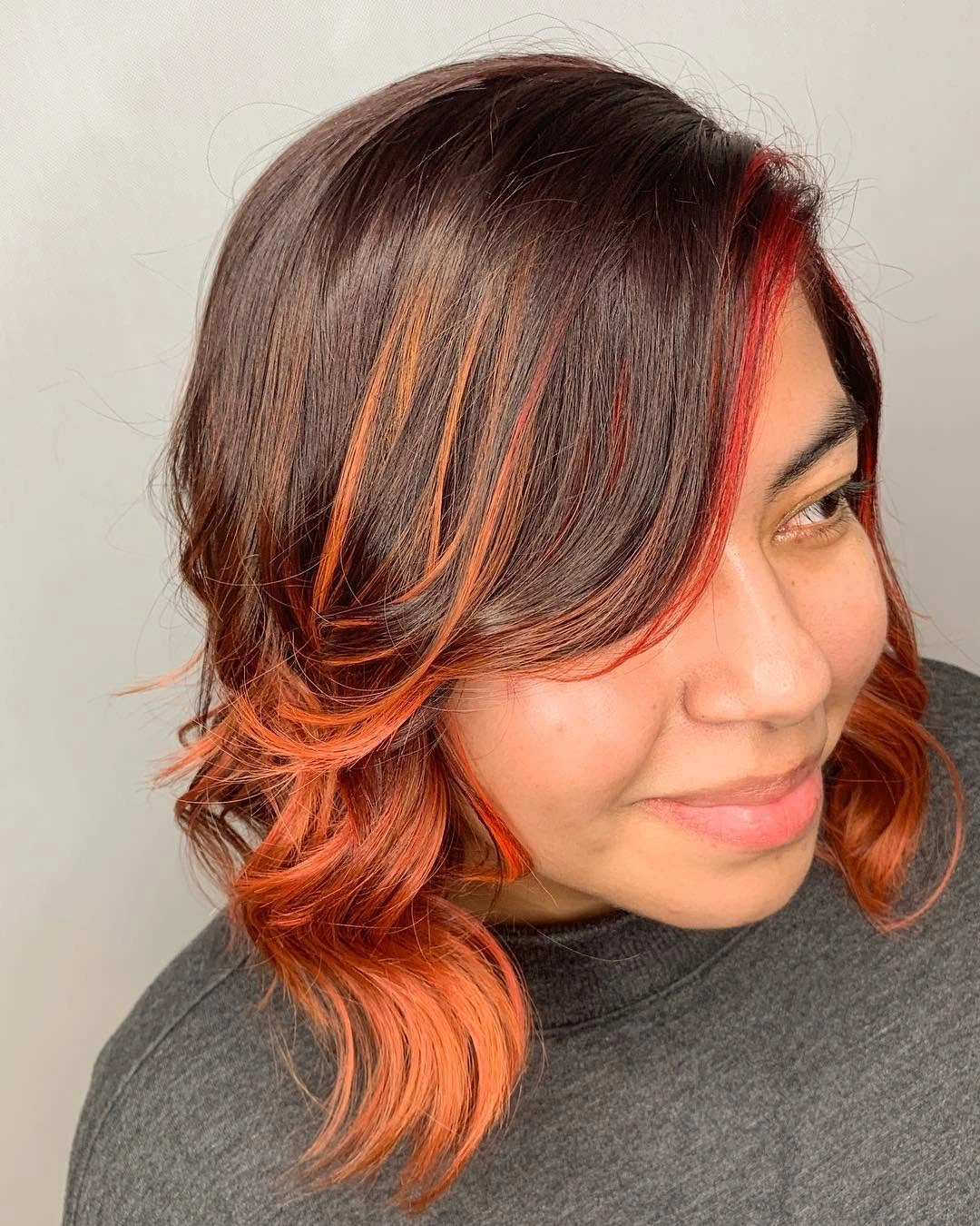 Brunette wavy bob with orange-red front streaks and curled ends