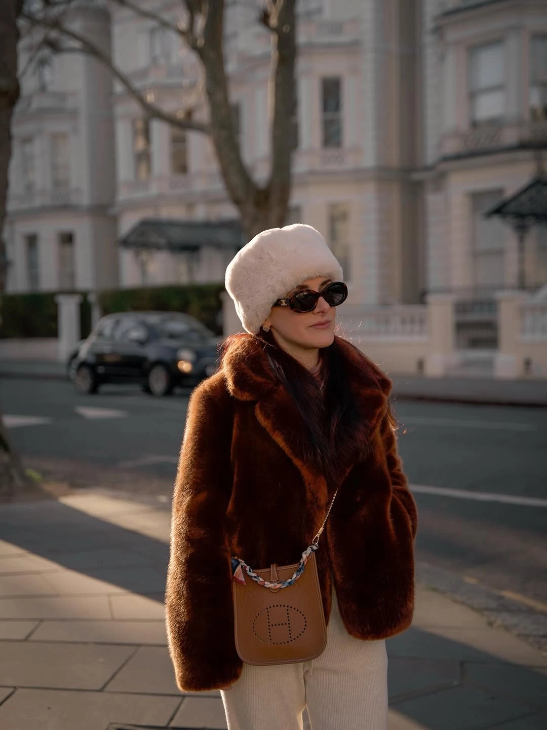 Dark brown textured jacket with cream trousers, knit cap, and small brown bag