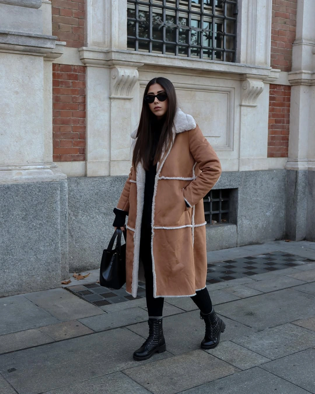Tan trimmed winter coat over black layers with lace-up boots and black bag