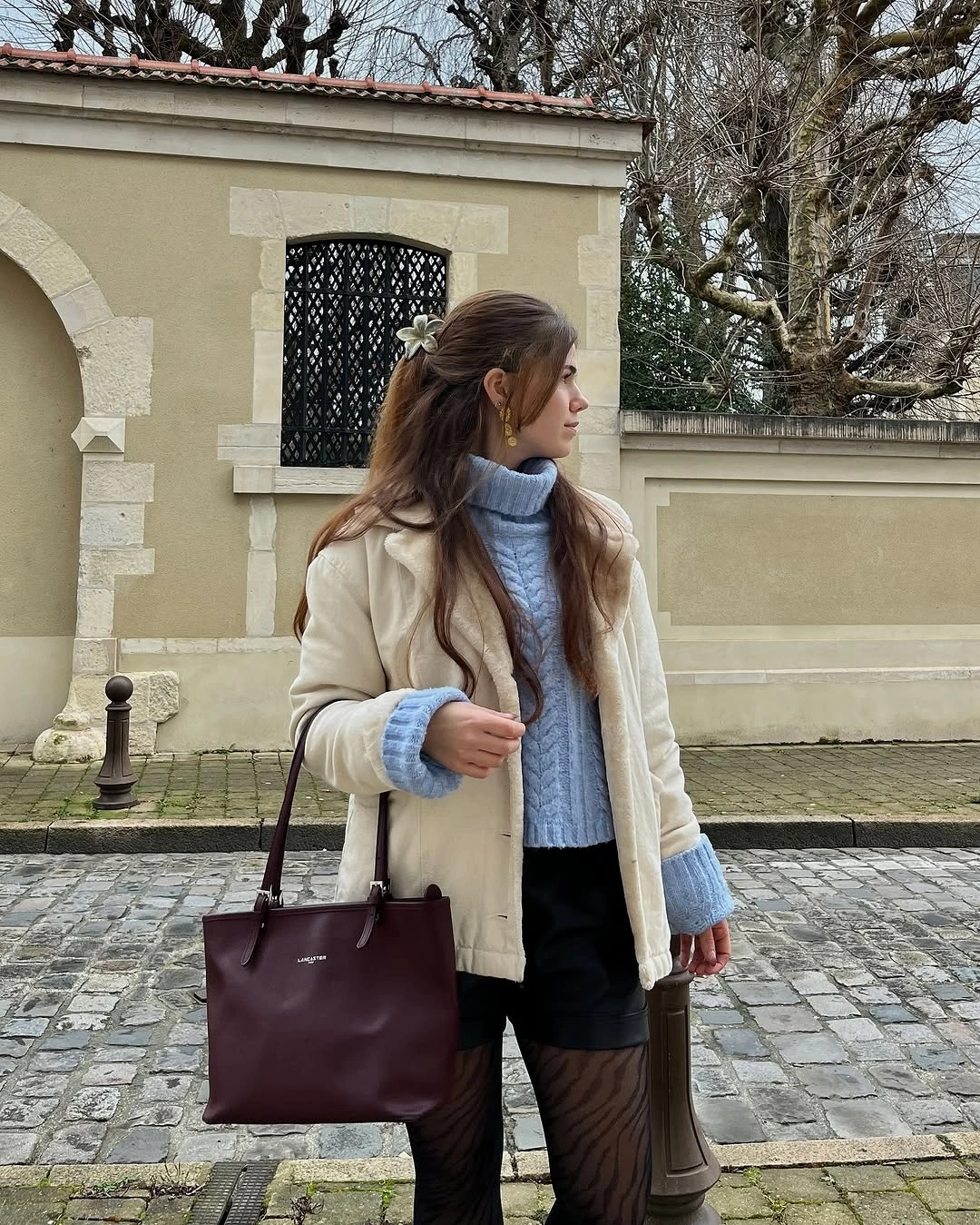 Cream coat with powder blue turtleneck, black skirt, tights, and burgundy tote