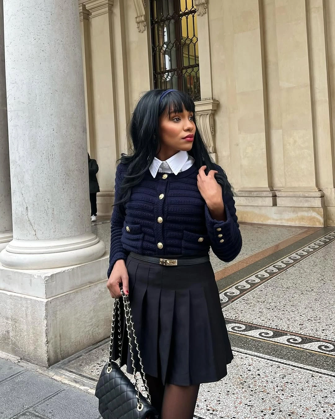 Navy padded jacket with white collar, gray pleated skirt, socks, and black bag