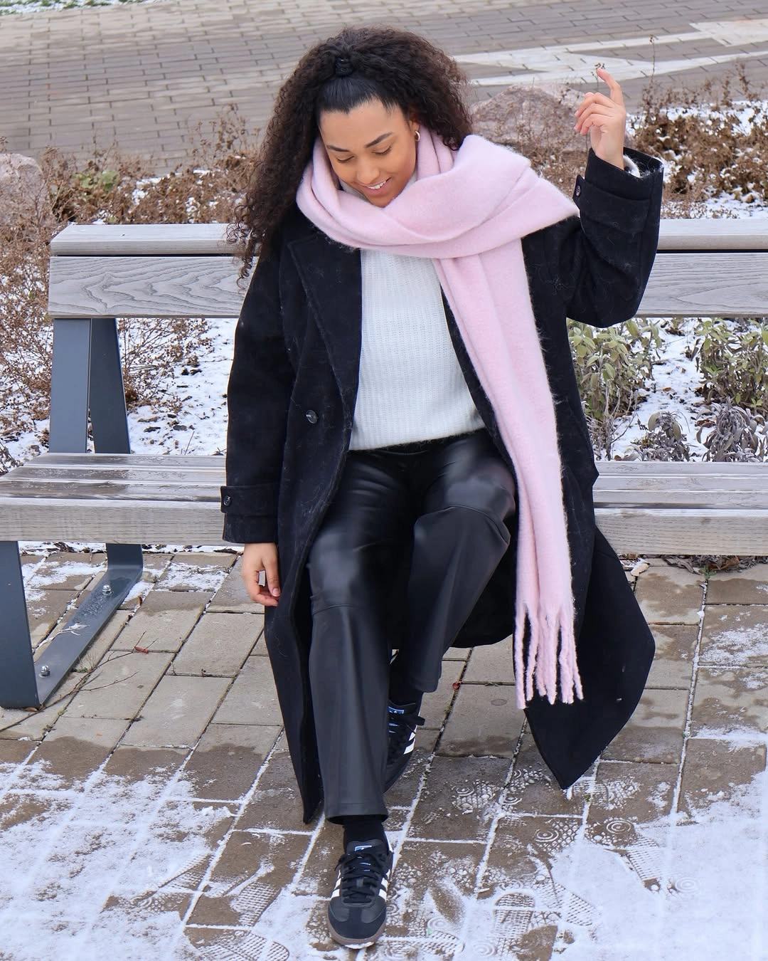 Black long coat with white knit, pink scarf, dark trousers, and loafers