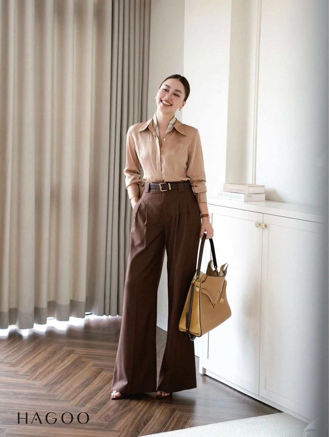 Tan collared shirt tucked into brown wide-leg trousers with a dark belt and ochre handbag.