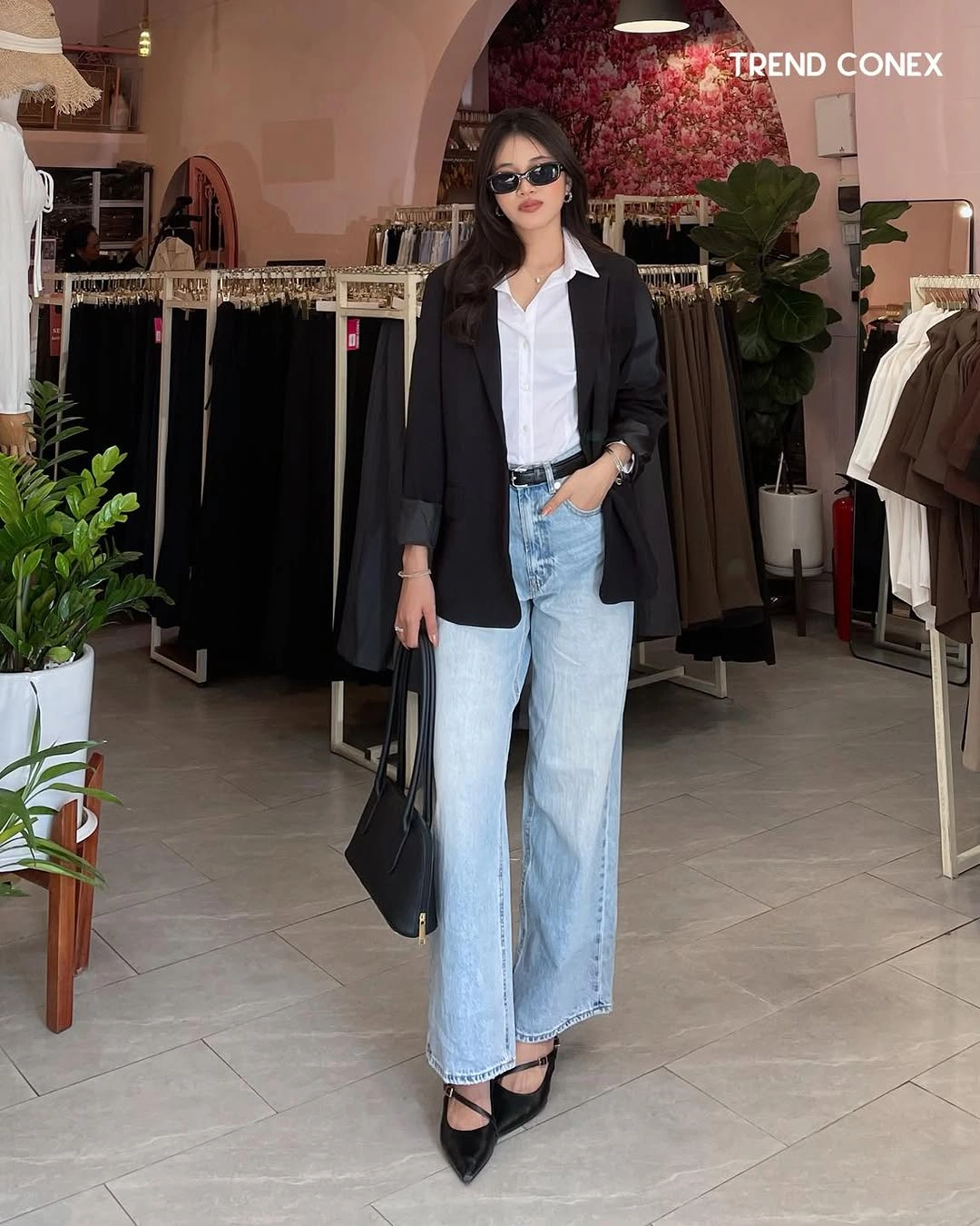 Black blazer over a white collared shirt and wide blue jeans with black strapped shoes.