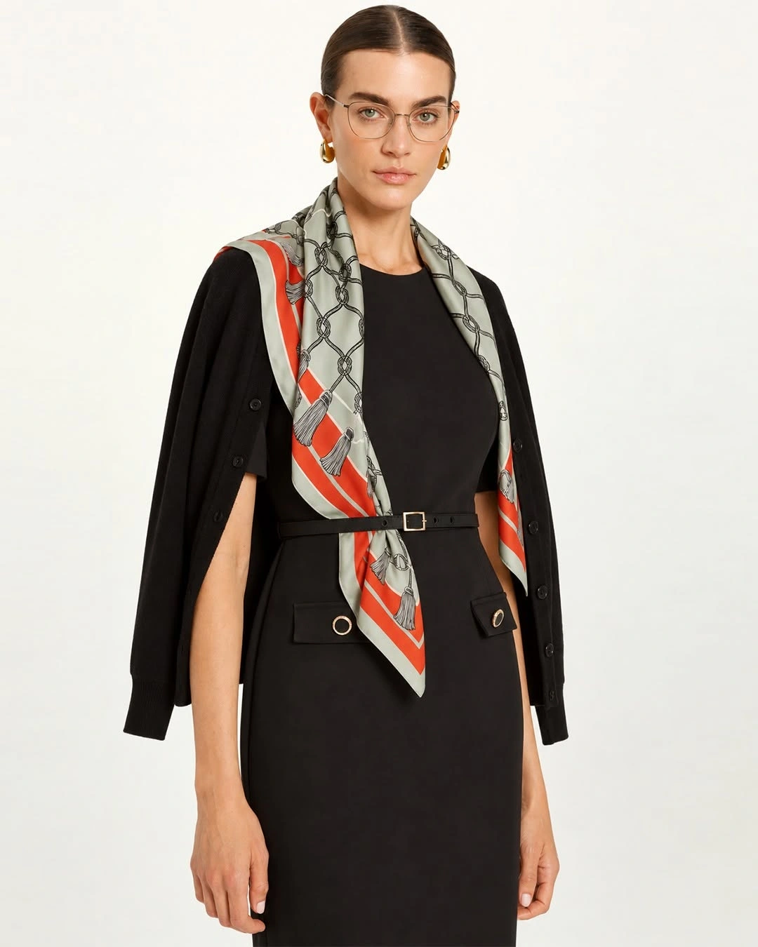 Black dress and draped cardigan with an orange-edged patterned scarf beneath a narrow black belt.