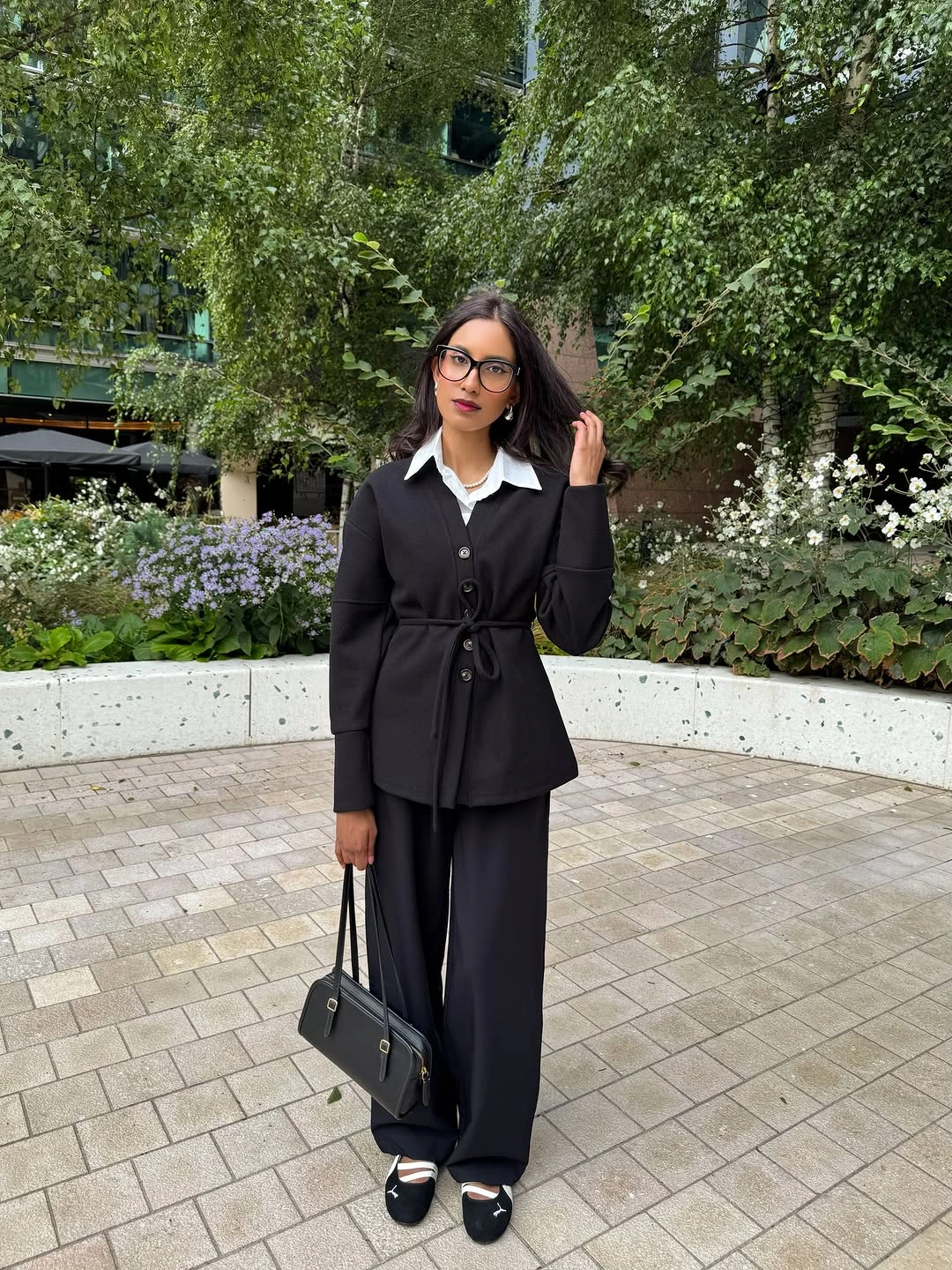 Waist-tied black button-front layer, white collar, wide black trousers, and low shoes with pale bands.
