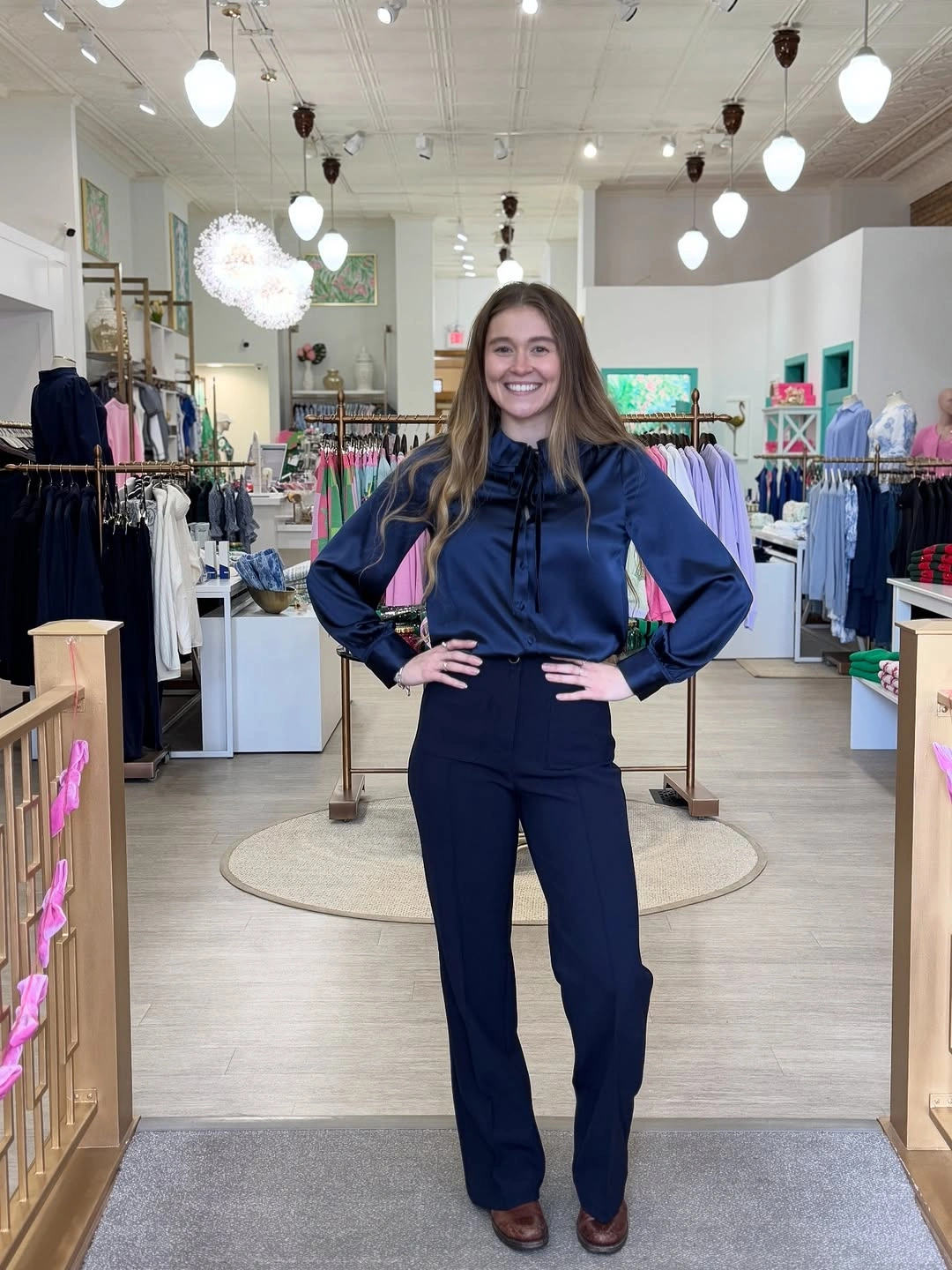 Reflective-looking navy tie-neck blouse with gathered cuffs, navy trousers, and brown shoes.