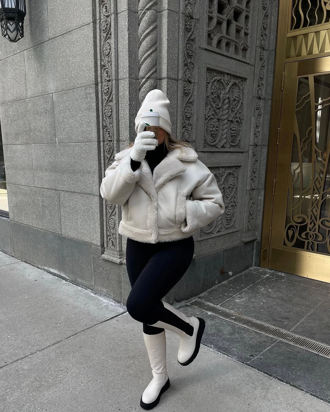 White cropped jacket with black leggings, white beanie, and tall boots