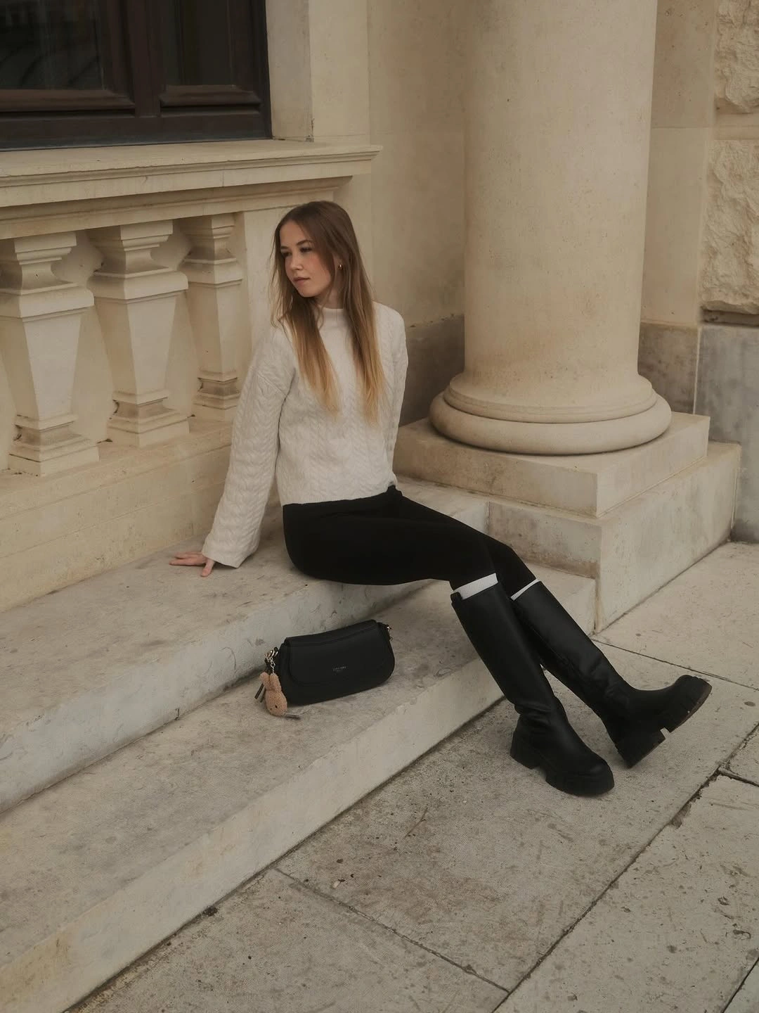 White textured sweater with black leggings and tall black boots