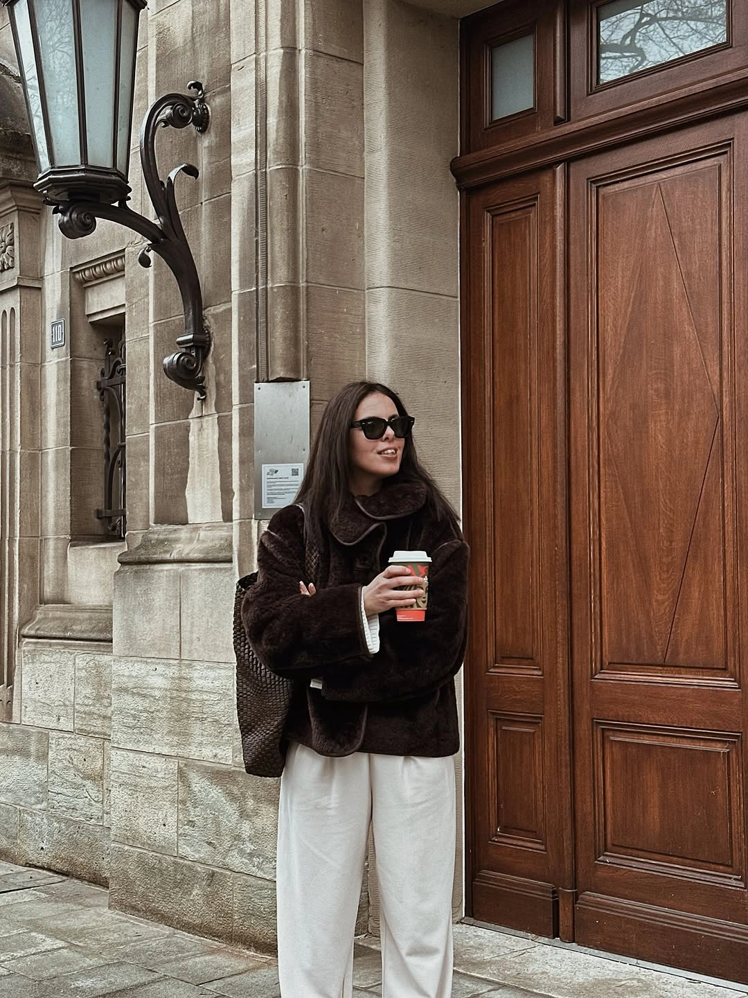 Short brown textured coat with white wide trousers and a dark bag