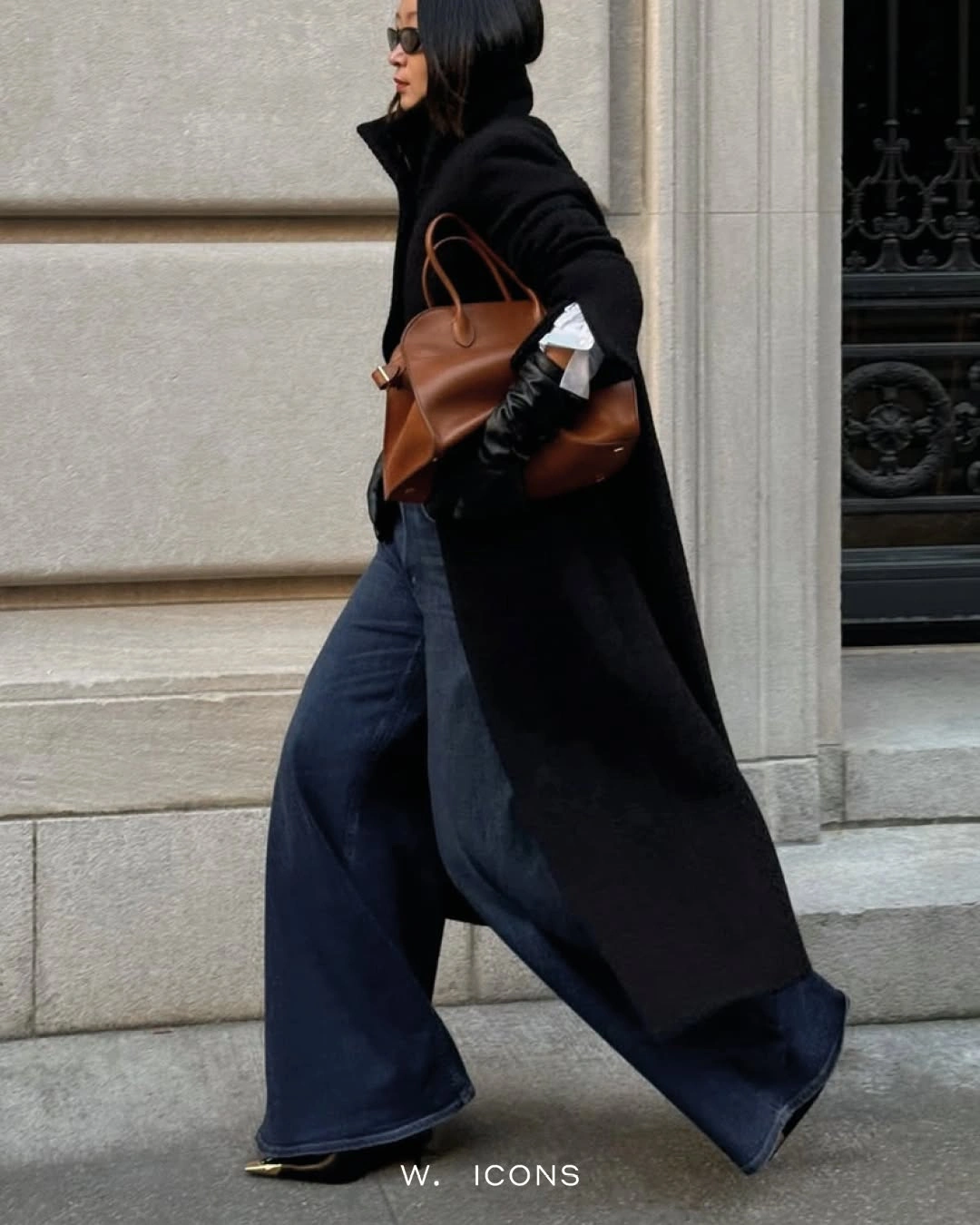 Long black coat, wide dark trousers, black boots, and brown bag