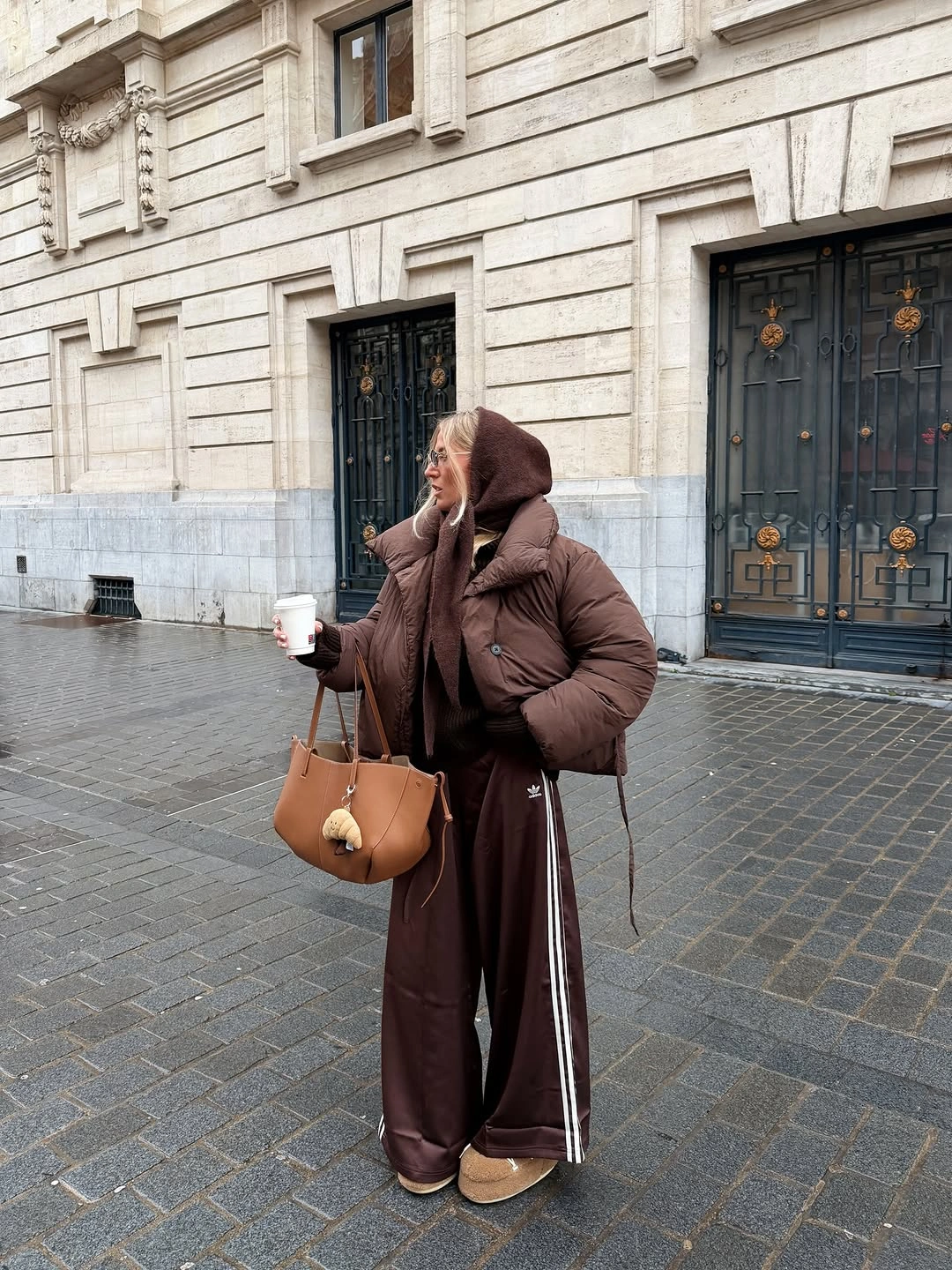 Brown puffer, striped burgundy-brown track pants, tan tote, and neutral shoes
