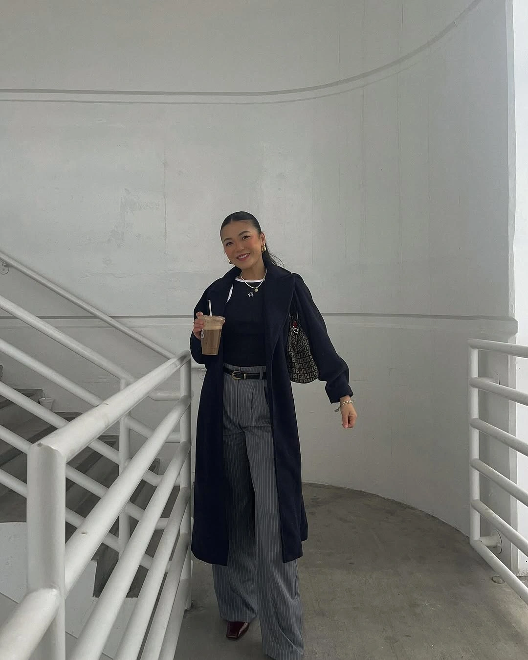 Navy long coat, black top, gray pinstriped trousers, and dark bag