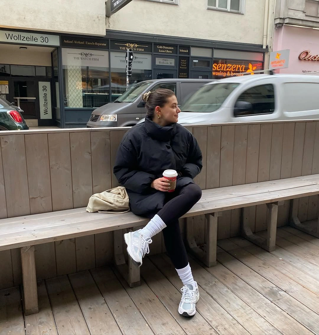 Black puffer outfit with white socks, white-gray sneakers, and beige bag
