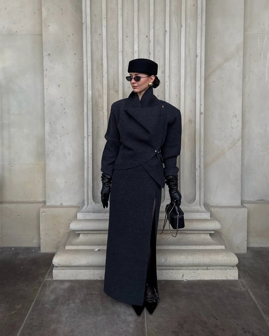 Dark high-neck outfit, black cap, sunglasses, gloves, and chain bag