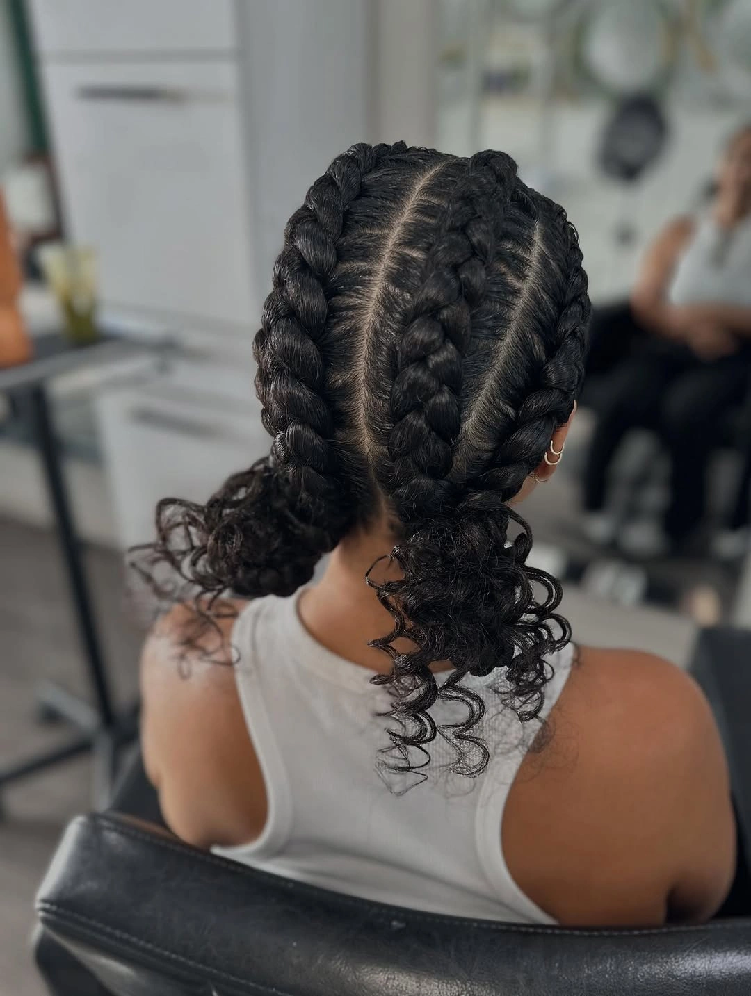 Thick dark scalp braids meeting two low gathered sections with loose spiral curls