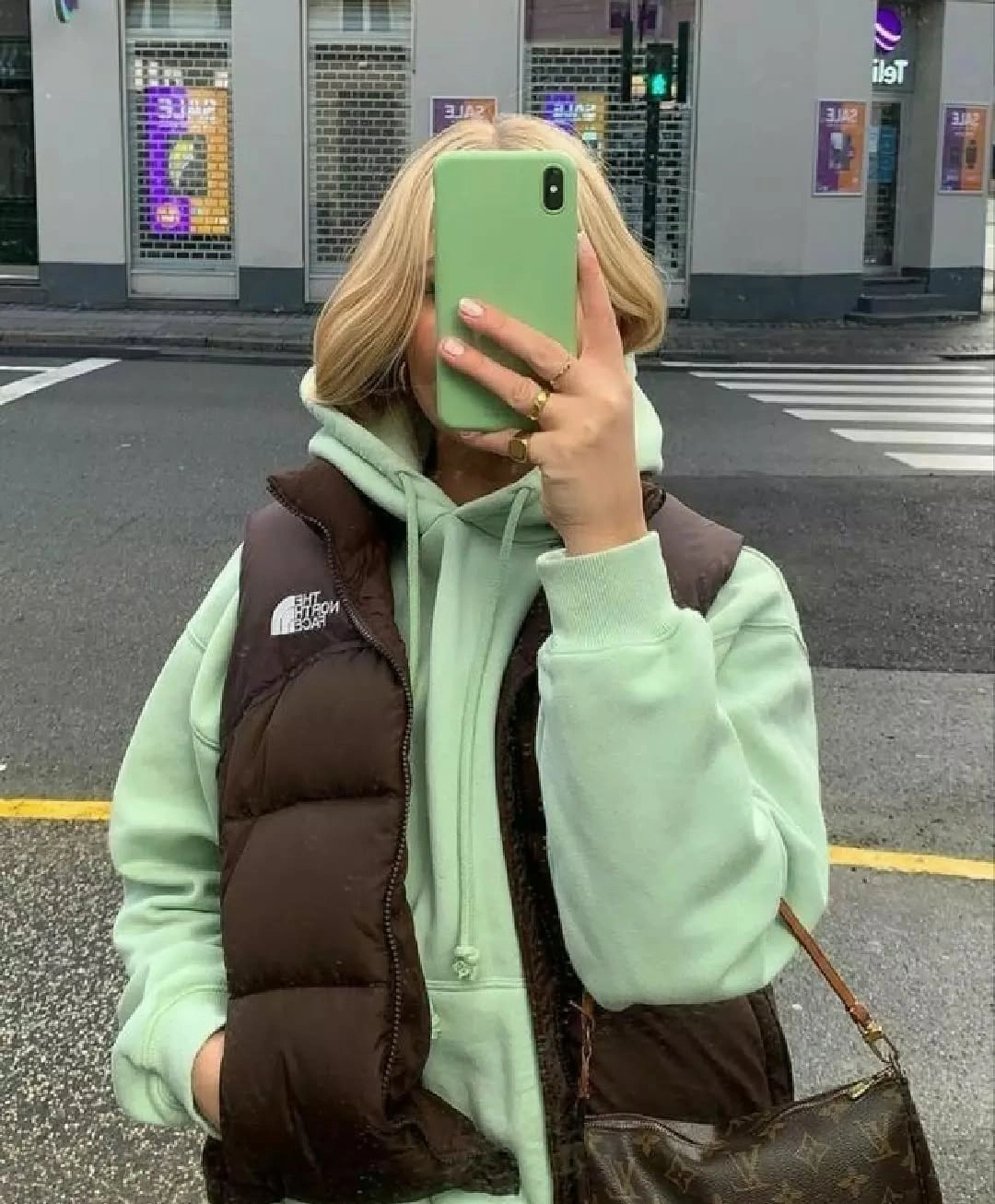 Mint hoodie under brown puffer vest with dark patterned crossbody bag