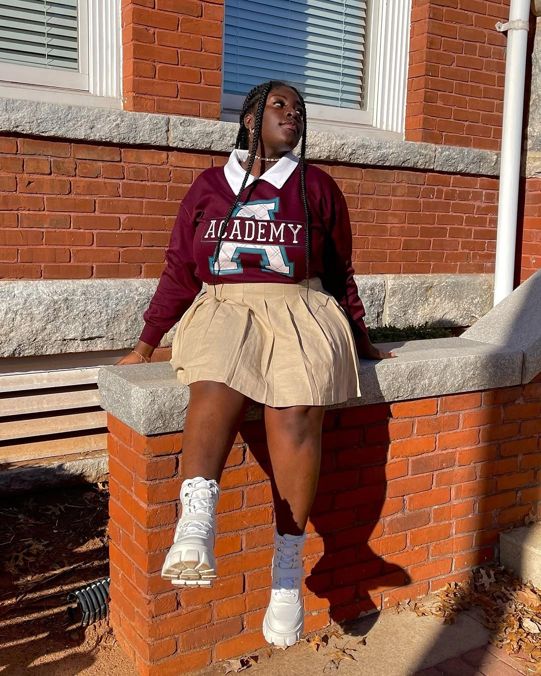 Burgundy graphic sweatshirt, white collar, beige pleated skirt, and white boots