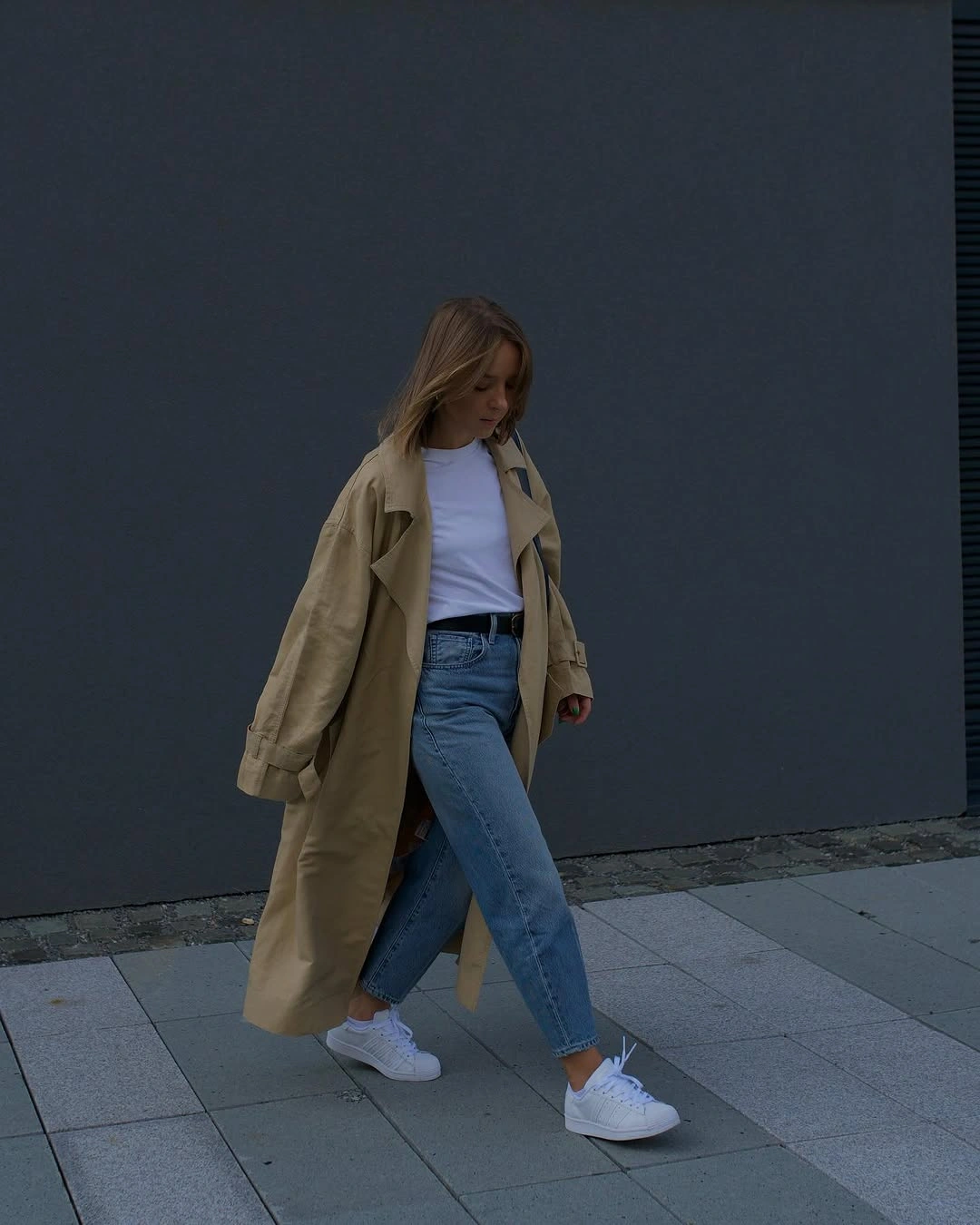 Beige trench over white tee and blue jeans with white sneakers