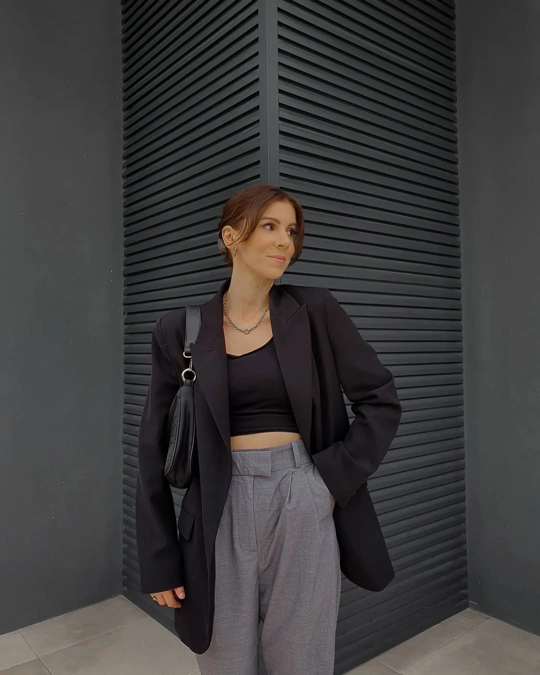 Black blazer and cropped top with gray pleated trousers and black bag