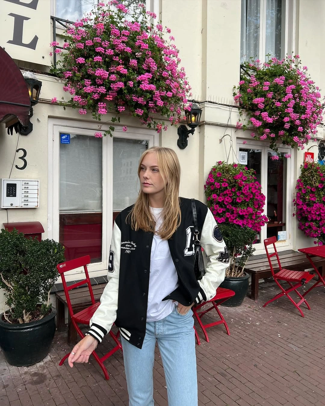 Black varsity-style jacket, white tee, light blue jeans, and dark bag