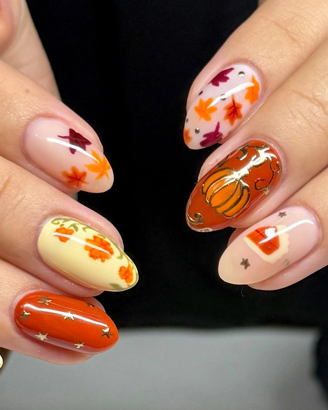 Almond nails with pumpkin-like motifs, leaves, stars and orange polish
