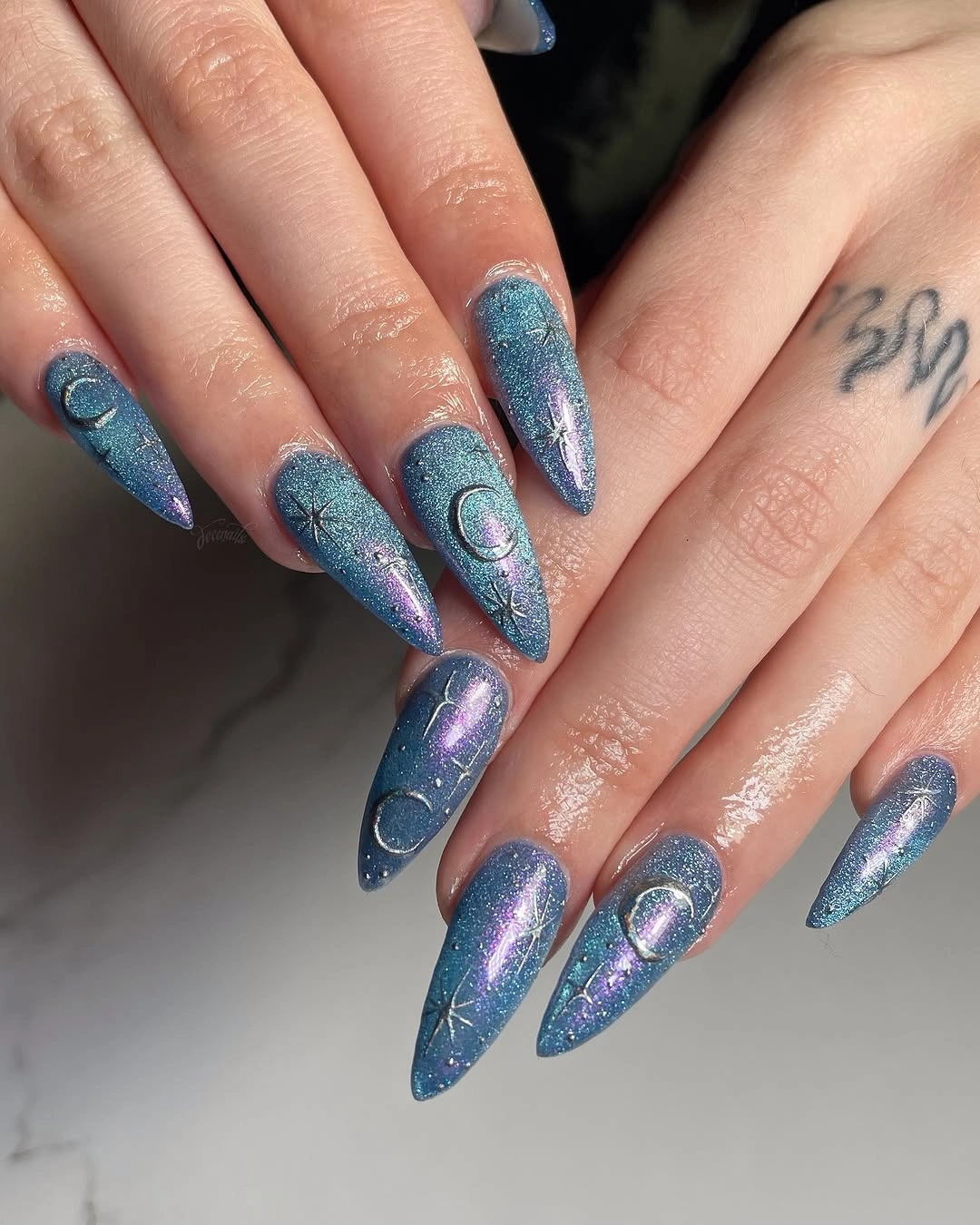 Long pointed blue-purple nails with crescent moons and star-like accents
