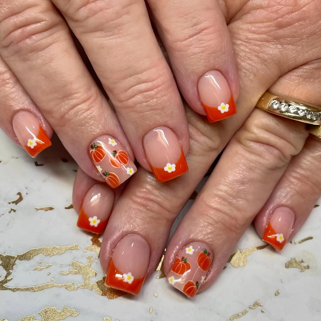 Short square nails with orange tips, flowers and pumpkin-like accents