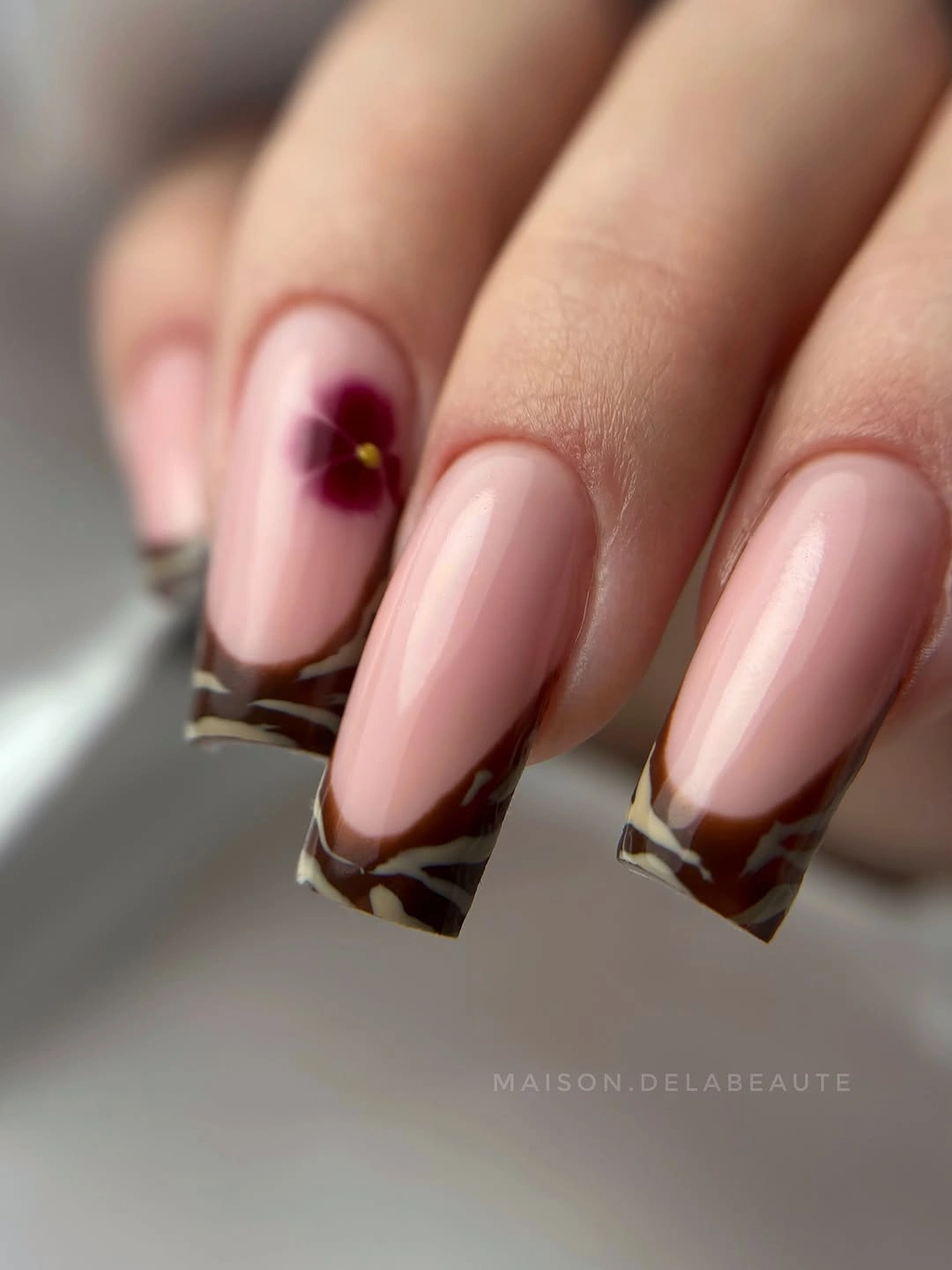 Square nude nails with brown tips and burgundy flower-like accent