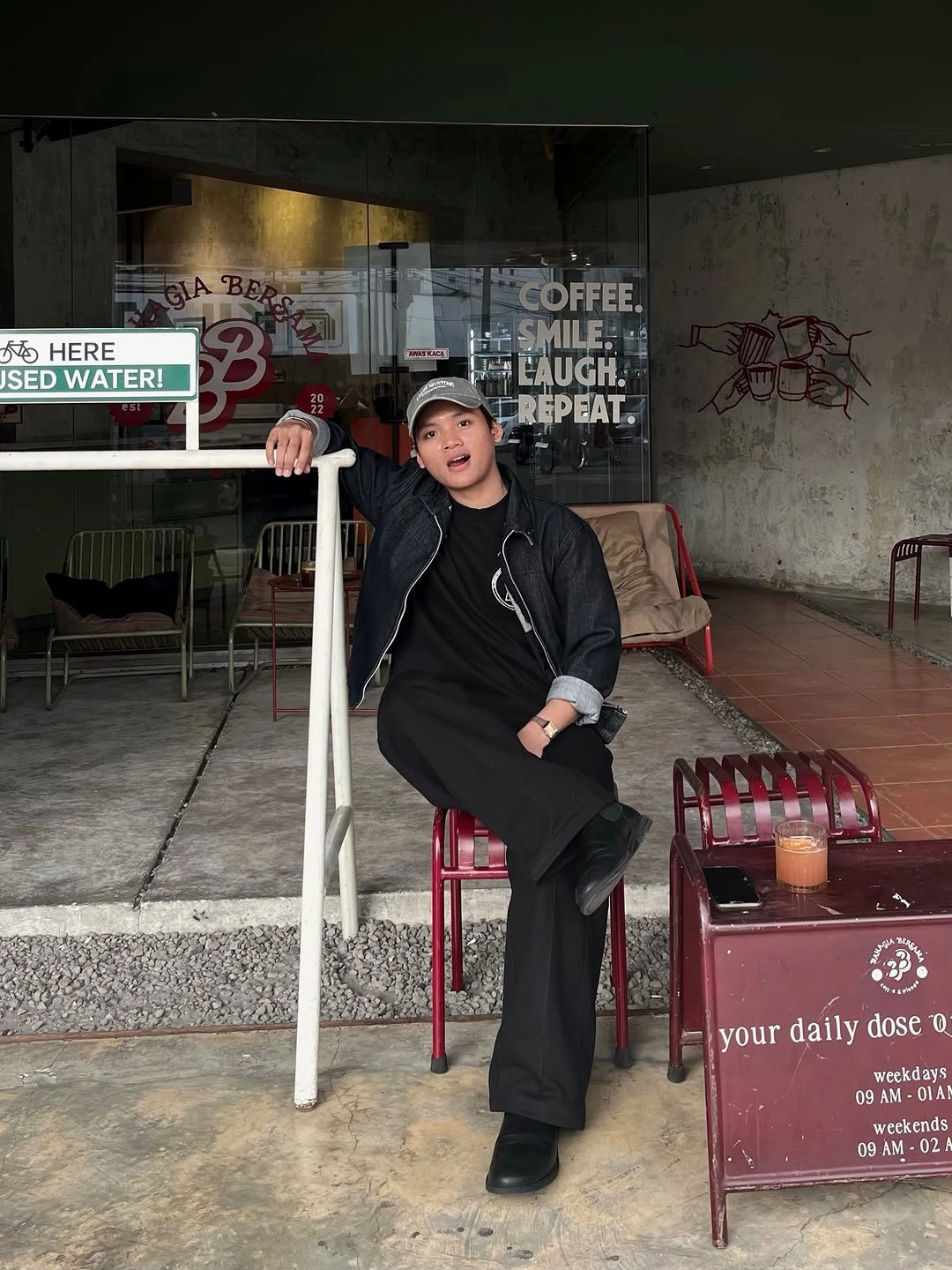 Relaxed all-black outfit with wide trousers, cap, and dark bag