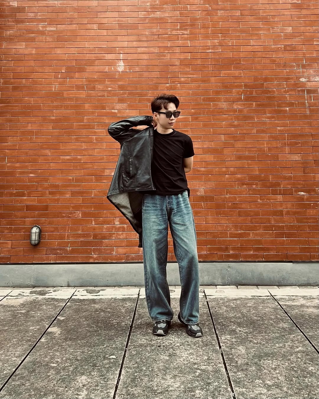 Black T-shirt and open jacket with wide blue jeans and dark shoes